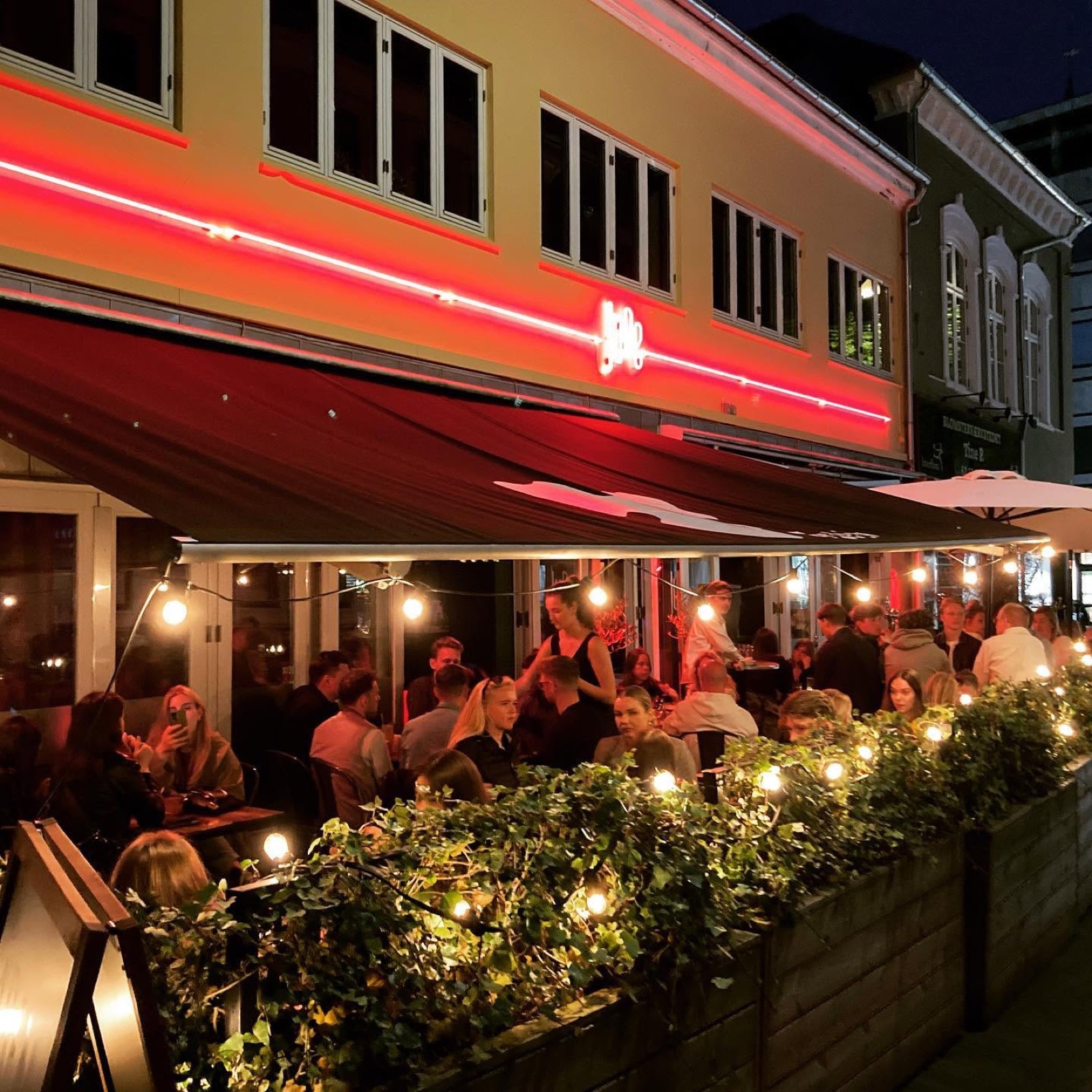 JUNEs terrasse med gæster, lyskæder og den oplyste facade
